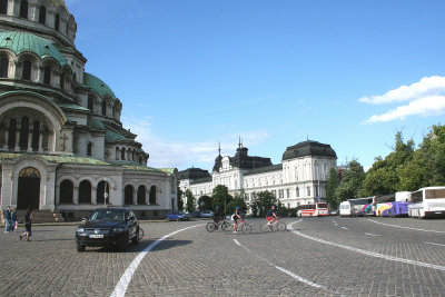 Cars, bikers and cobblestone streets in front of the cathedral.