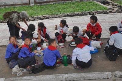 Schoolkids eating lunch on the sidewalk NKorea