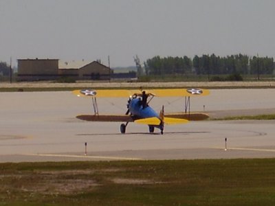 A guy about to stand on the biplane before transferring to a helicopter skid in mid-air
