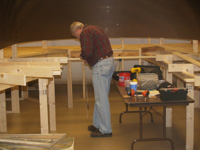 Using a plumb bob to align the ned of the benchwork studs to the fascia line drawn on the floor.