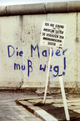 A dated photo of a Checkpoint Charlie sign with graffiti on the Berlin Wall behind it.