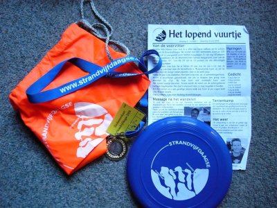 Parafernalia Strandvijfdaagse: rugzakje, keycord, deelnemerskaart, medaille, dagblad Het lopend vuurtje en een frisbee.