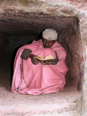 A priest reads in a nook carved into the stone wall surrounding the churches.