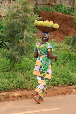 A Rwandan woman wearing colorful traditional clothing carries produce.