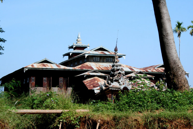 A dilapidated building on the river bank with a rusty metal roof.