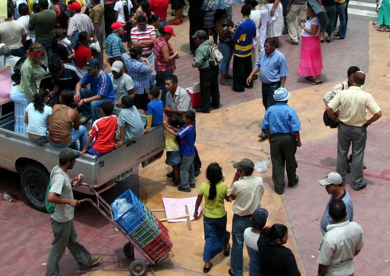 A pickup truck loaded with people and a man going by with a hand cart.