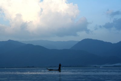 A lone man on a boat with mountains behind him.