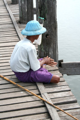 A fisherman is sitting on the bridge patiently fishing in Taungthaman Lake.