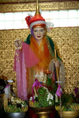 A colorful statue at the Botahtaung Pagoda with offerings of fruit in front of it.