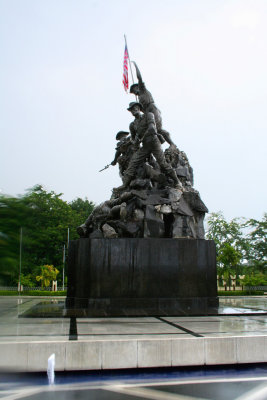 Closeup of the Tugu Negara  with the Malaysian flag flying over it.