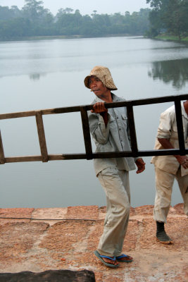 A Cambodian worker at the Angkor Wat Temple causeway carrying a ladder.