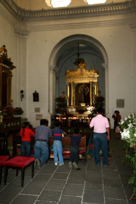 Worshippers praying in front of a side altar inside of La Merced.
