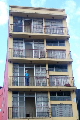 A lone man standing on the balcony of a deserted-looking apartment building on Avenida 2 in San Jos.