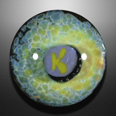 A sculpted K, all dressed up, sits over top of a bed of frit.  Another K is seen on the backside.
