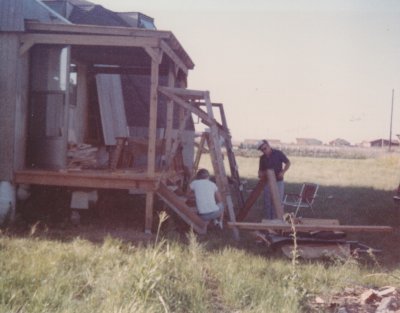 Installing the steps up to the back porch. Have George and Nola moved in and planted corn in the field across the street?