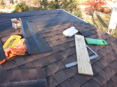I used the old towel to wipe off water and leaves, and the board and framing square to cut the shingles. Because it was cool, the plastic strips covering the adhesive on the back came off easier than in my past experience, and I pulled off all to help keep the shingles in place in the wind.