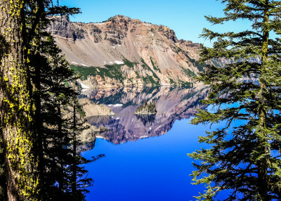 Calm early morning waters reflect the lake rim and the Phantom Ship formation in Crater Lake National Park