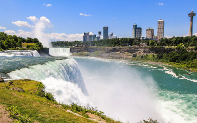 Both falls flowing into Niagara Gorge with Niagara Falls Canada towering above, from Prospect Point