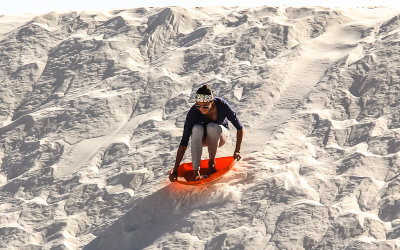 A woman sleds down a dune in White Sands National Monument