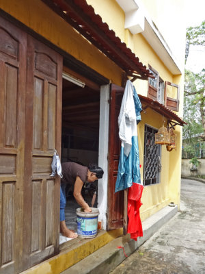 Woman cleaning the front entrance of her house - next photo shows bird cages seen here - Old Town, Hoi An, Vietnam