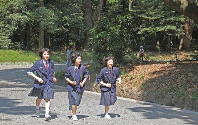 Schoolgirls approaching the Meiji Shinto Shrine inner complex on the gravel road entrance surrounded by cedars.- Tokyo