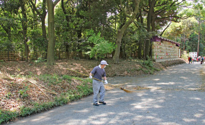Worker on the gravel road to and from the Meiji Shrine. Sake barrels are in the background on the left side of the road.