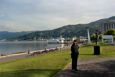 Judy near Lake Suwa with a cartoonish swan boat in the background - in Suwa-shi