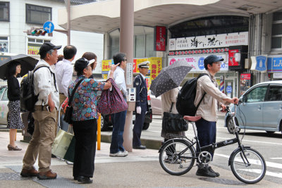 Pedestrians wait for a signal from the man in unform for permission to cross the street - front of the Omi-cho Market in Kanaawa