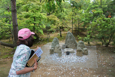 Judy tossing coins at Jizo Buddhist statues for good luck - on the grounds of the Temple complex (Rokuon-ji) in Kyoto