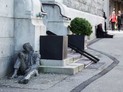 En oppgitt person skapt av Mland p Os sitter lett henslengt p gaten - litt bortenfor sitter en utholdende tigger.Tigger i Ber