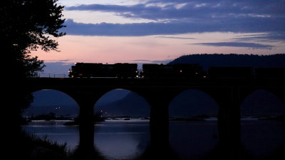  A NS SD70Ace is silhouetted against the setting sun as it leads a Westbound train across the famous stone arches of the bridge 