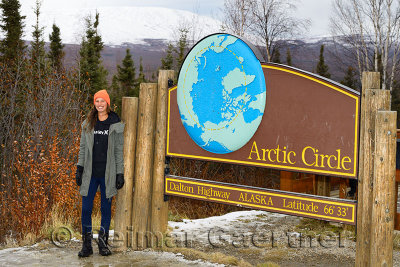 Female tourist standing by the sign board for the Arctic Circle along the Dalton Highway in Alaska