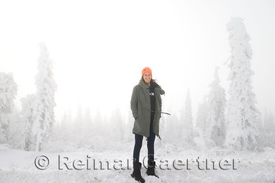 Female tourist on a snowbank with snow covered trees on the Dalton Highway Alaska