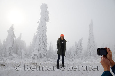 Young woman on a snowbank being photographed with snow covered trees on the Dalton Highway Alaska
