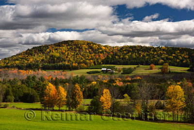 Farmhouse among green fields and forest trees in Fall color on Blue Mountain Vermont