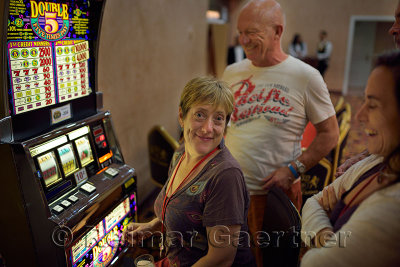 Group of friends laughing while watching smiling woman play a slot machine at a casino