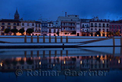 Bell tower of Saint Ana church with houses on Betis street Seville reflected at dawn in Alfonso XIII Canal