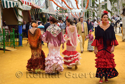 Women in flamenco dresses walking on ochre earth at the April Fair in Seville