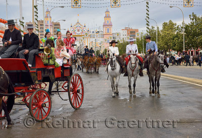 Mule drawn carriages and horseback riders on Antonio Bienvenida street with Main Gate 2015 Seville April Fair