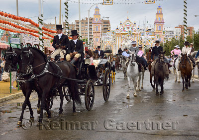 Horse drawn carriages and women on horseback riding sidesaddle on Antonio Bienvenida street with Main Gate 2015 Seville April Fa
