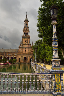 Painted ceramic railing and lamp posts along canal with South Tower at Plaza de Espana Seville Spain