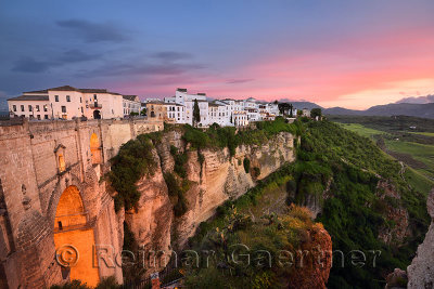 Red sky evening light on white buildings and orange cliffs at El Tajo Gorge Ronda Spain