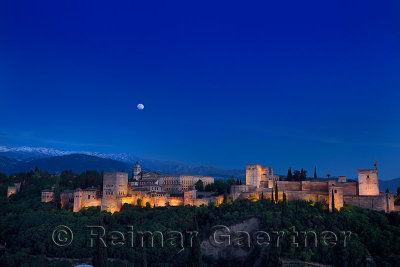 Moonrise over lit Alhambra Palace Complex Granada at twilight with Sierra Nevada Mountains