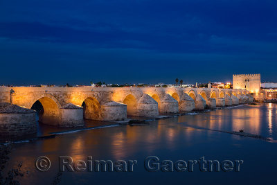 Lights reflected in the Guadalquivir river from the Roman Bridge and Calahorra Tower at dusk Cordoba