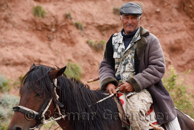 Kazakh on horseback tending sheep at red rock formations Sarytau mountains Assy Plateau Kazakhstan