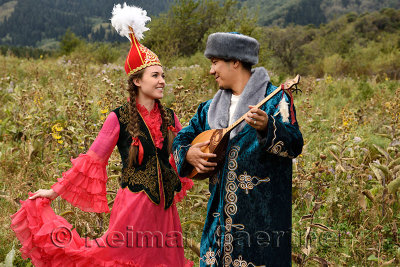 Man playing dombra and woman in traditional Kazakh dress in a field at Huns village Kazakhstan