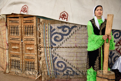 Woman in traditional Kazakh dress grinding wool for felt next to a yurt at Huns village Kazakhstan