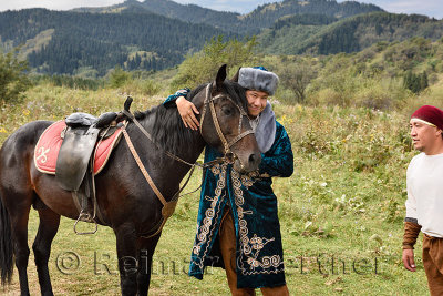 Man in traditional shapan overcoat and Borik cap hugging a stallion at Huns village Kazakhstan