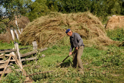Kazakh man using a scythe to mow grass with stacks of hay in Saty village Kazahkstan