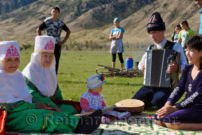 Grandmothers with baby and father playing accordion in traditional garb at a picnic in Saty Kazakhstan